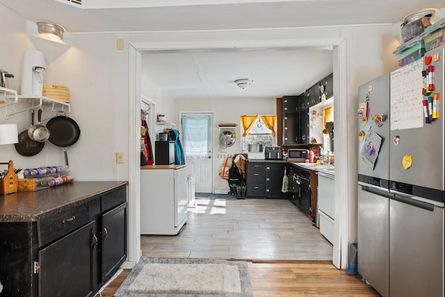 kitchen featuring dark cabinets, light wood-style floors, freestanding refrigerator, dark countertops, and washer / dryer