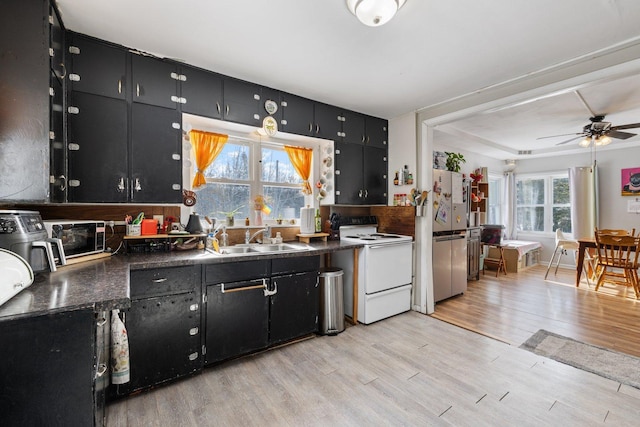 kitchen with electric range, freestanding refrigerator, dark cabinetry, light wood-style floors, and a sink