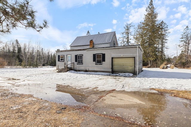 snow covered house featuring an attached garage, metal roof, and entry steps