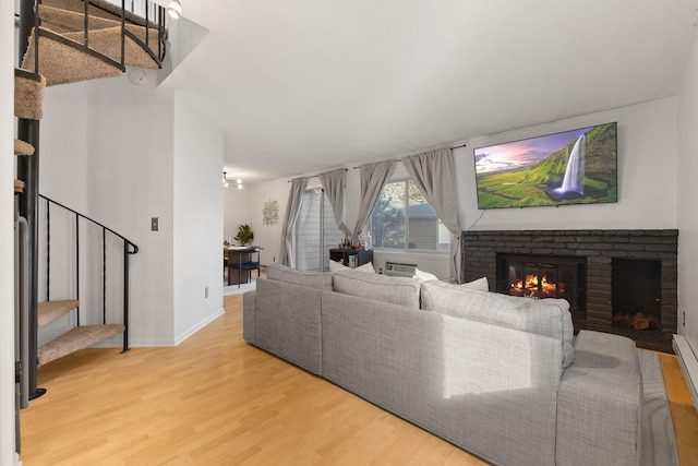 living room with a brick fireplace, stairs, baseboards, and light wood finished floors