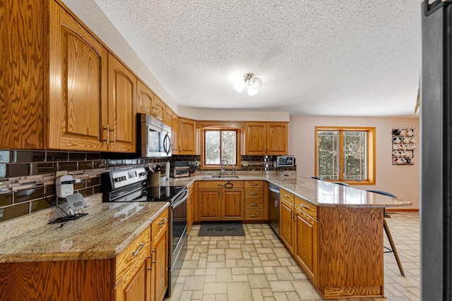 kitchen with sink, appliances with stainless steel finishes, a kitchen breakfast bar, kitchen peninsula, and light stone countertops