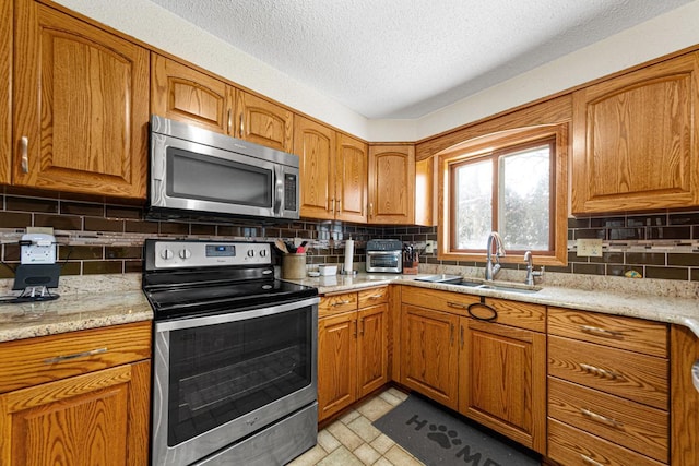 kitchen with appliances with stainless steel finishes, light stone countertops, sink, and decorative backsplash