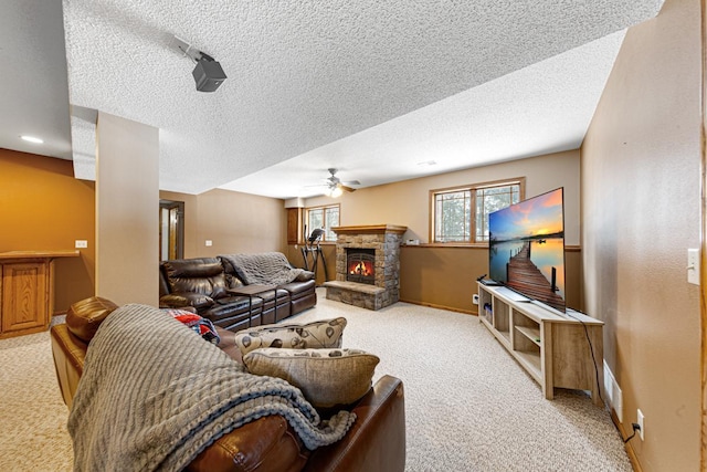 carpeted living room with a stone fireplace, a textured ceiling, and ceiling fan