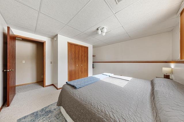 carpeted bedroom with a paneled ceiling and a closet