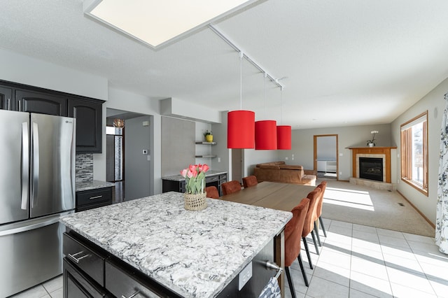 5078 Nicklaus Dr NW, Rochester, MN 55901 - kitchen featuring freestanding refrigerator, track lighting, light tile patterned floors, a fireplace with raised hearth, and light colored carpet