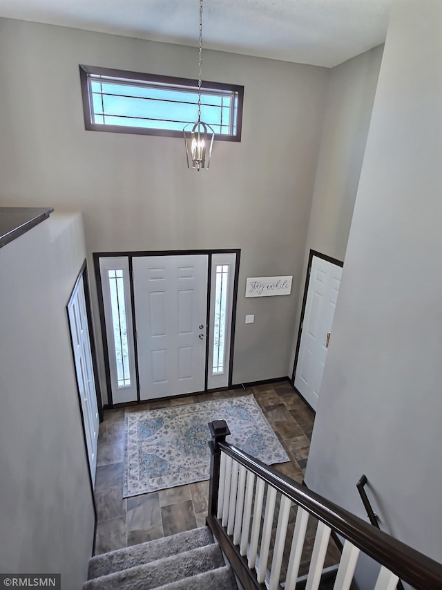 foyer entrance featuring stone finish floor, stairway, a towering ceiling, and an inviting chandelier