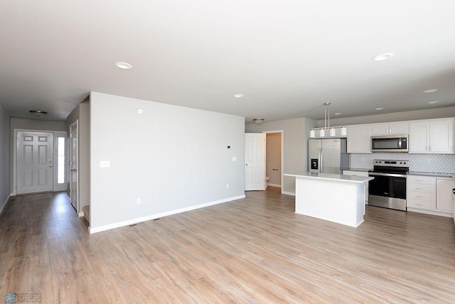 kitchen featuring appliances with stainless steel finishes, pendant lighting, white cabinetry, a center island, and light hardwood / wood-style floors