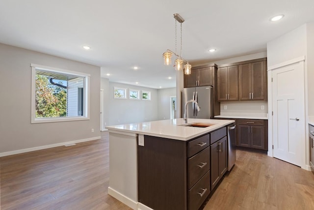 kitchen featuring appliances with stainless steel finishes, decorative light fixtures, an island with sink, and light wood-type flooring