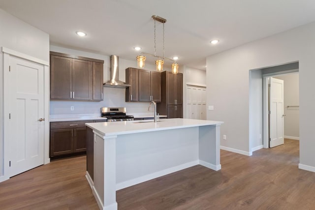 kitchen featuring pendant lighting, dark wood-type flooring, a kitchen island with sink, stainless steel range oven, and wall chimney exhaust hood