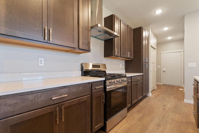 kitchen with dark brown cabinetry, wall chimney range hood, gas range, and light hardwood / wood-style floors