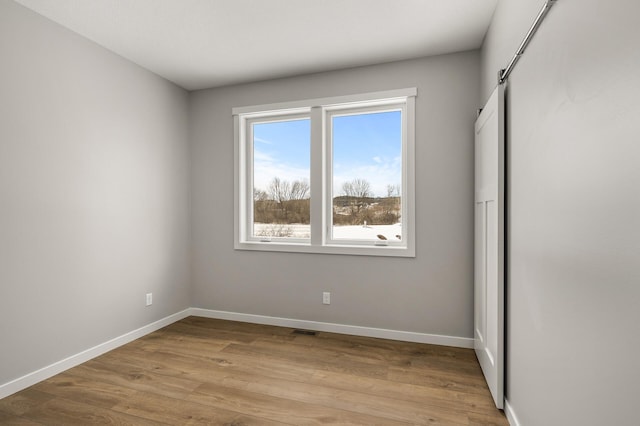 unfurnished bedroom featuring a barn door and light hardwood / wood-style flooring