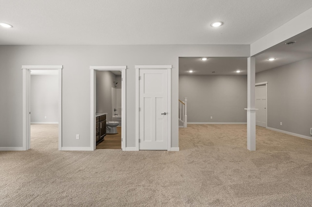 interior space with ensuite bath, light colored carpet, and a textured ceiling