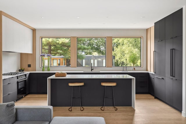 kitchen with a kitchen island, a breakfast bar, sink, stainless steel appliances, and light hardwood / wood-style flooring