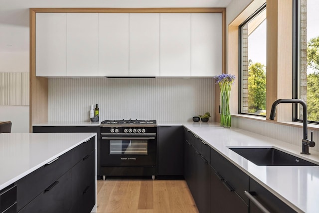 kitchen featuring black gas range oven, sink, dishwasher, white cabinets, and light wood-type flooring