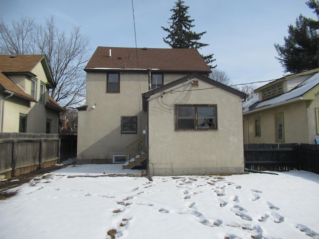 snow covered rear of property featuring fence and stucco siding