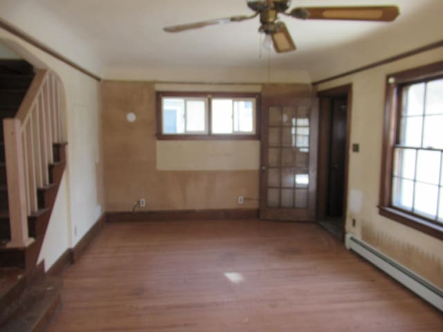 interior space featuring a baseboard radiator, wood finished floors, a ceiling fan, baseboards, and stairs