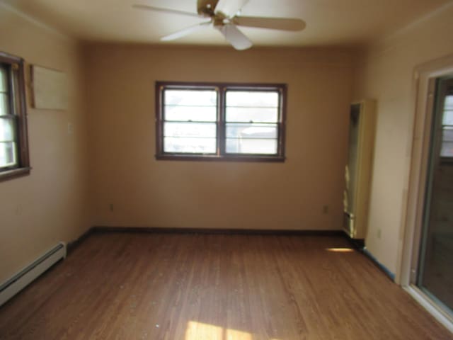 empty room with a ceiling fan, a baseboard radiator, baseboards, and wood finished floors