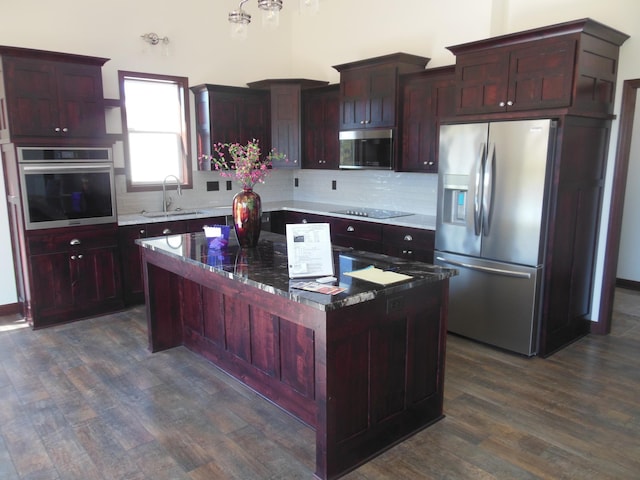 kitchen with sink, appliances with stainless steel finishes, tasteful backsplash, a kitchen island, and dark hardwood / wood-style flooring