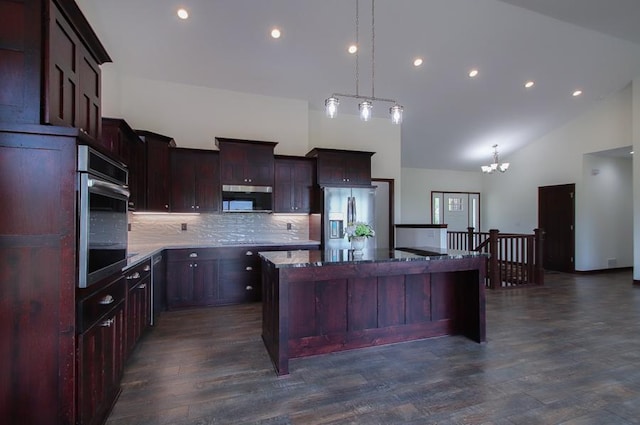 kitchen with pendant lighting, dark wood-type flooring, a kitchen island with sink, stainless steel appliances, and light stone countertops