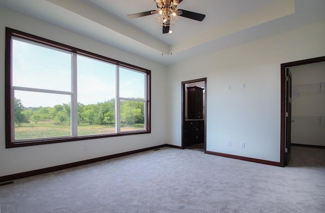 carpeted empty room featuring ceiling fan and a raised ceiling