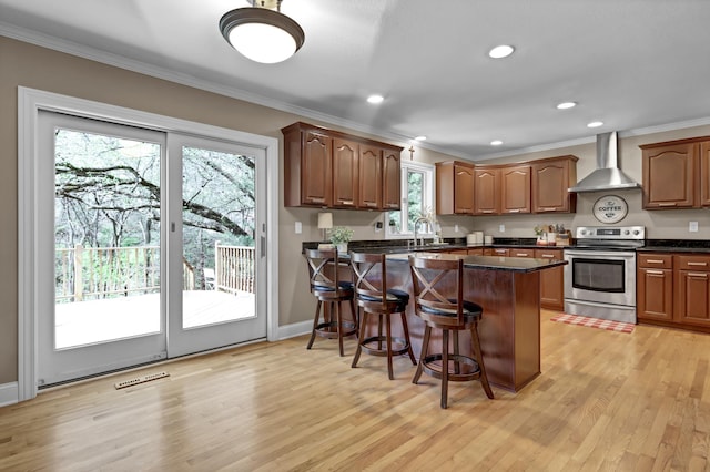 kitchen featuring visible vents, electric stove, ornamental molding, wall chimney exhaust hood, and a kitchen bar