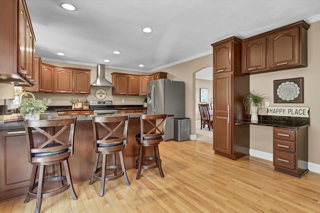 kitchen with arched walkways, stainless steel appliances, ornamental molding, wall chimney range hood, and a kitchen bar