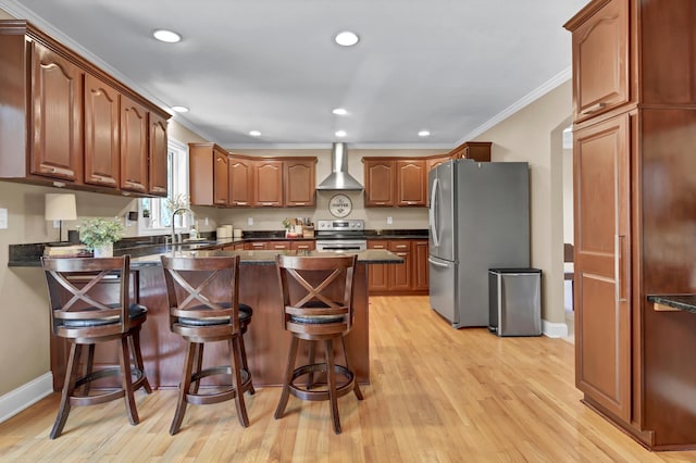 kitchen with stainless steel appliances, a kitchen breakfast bar, ornamental molding, brown cabinets, and wall chimney exhaust hood