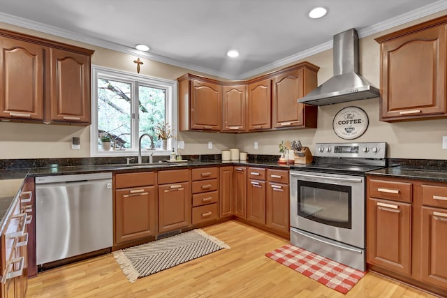 kitchen featuring a sink, appliances with stainless steel finishes, wall chimney exhaust hood, light wood finished floors, and crown molding