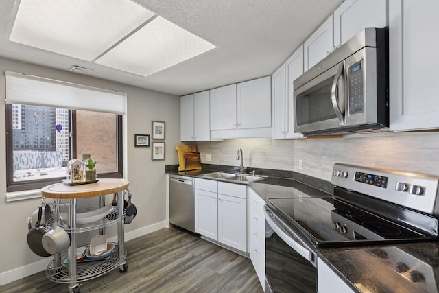 kitchen with appliances with stainless steel finishes, dark hardwood / wood-style floors, white cabinetry, sink, and backsplash