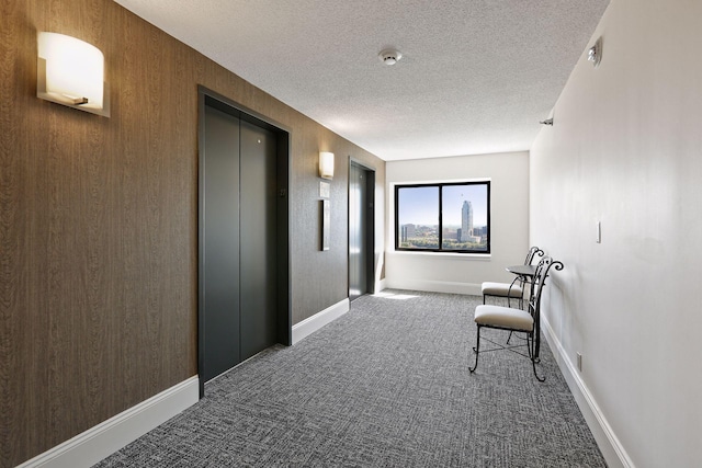 corridor with elevator, a textured ceiling, and dark colored carpet