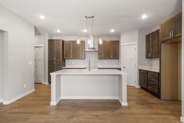 kitchen with pendant lighting, sink, a center island with sink, and wall chimney range hood