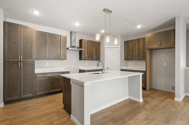 kitchen with sink, hanging light fixtures, a kitchen island with sink, light hardwood / wood-style floors, and wall chimney exhaust hood