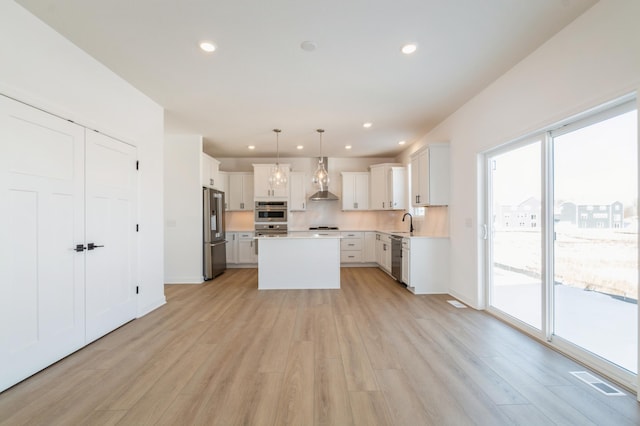 kitchen with white cabinetry, hanging light fixtures, stainless steel appliances, light hardwood / wood-style floors, and a kitchen island