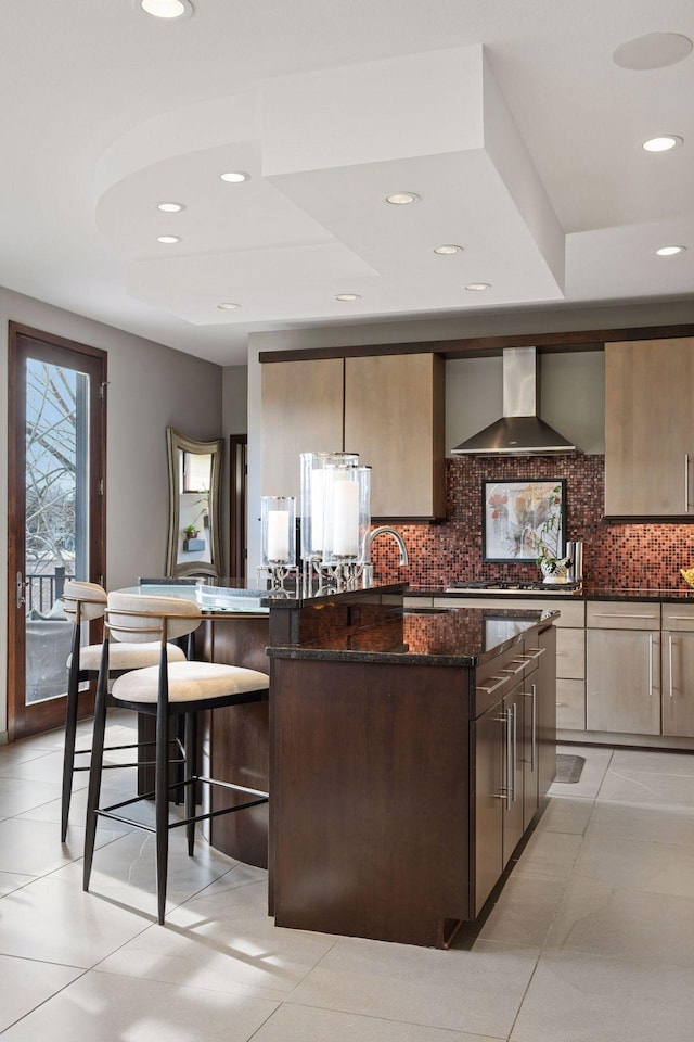 kitchen with tasteful backsplash, a large island, modern cabinets, dark stone countertops, and wall chimney range hood