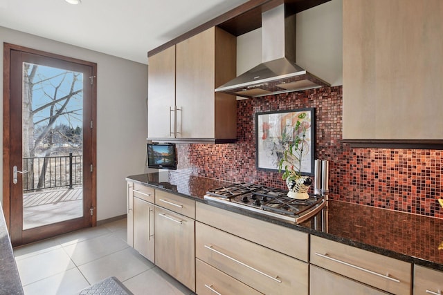 kitchen with wall chimney range hood, stainless steel gas stovetop, decorative backsplash, and dark stone countertops