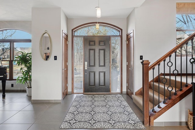 tiled entrance foyer featuring stairway, a wealth of natural light, and baseboards