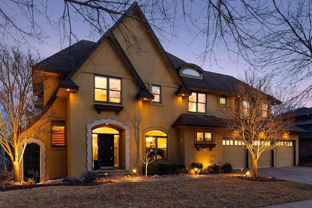 view of front facade featuring stucco siding, driveway, a shingled roof, and a garage