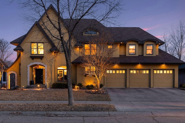 french country home with stucco siding, an attached garage, and concrete driveway