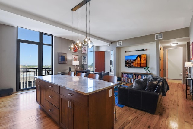 kitchen featuring a kitchen island, a kitchen bar, hanging light fixtures, light hardwood / wood-style floors, and light stone countertops