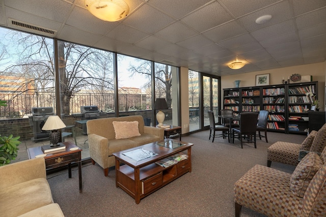 carpeted living room with a wall of windows and a drop ceiling