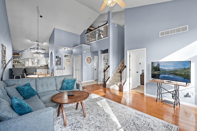 living area featuring baseboards, visible vents, stairway, light wood-type flooring, and high vaulted ceiling