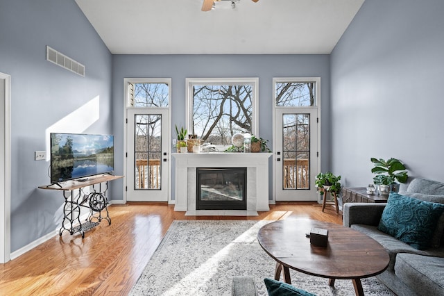 living area with visible vents, light wood-style flooring, a fireplace with flush hearth, ceiling fan, and baseboards