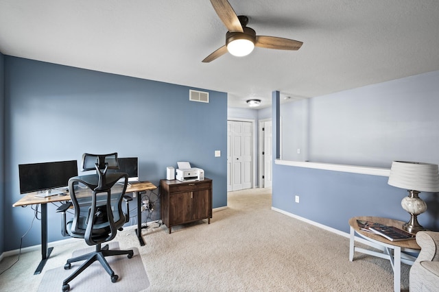 office area featuring a textured ceiling, light colored carpet, a ceiling fan, visible vents, and baseboards