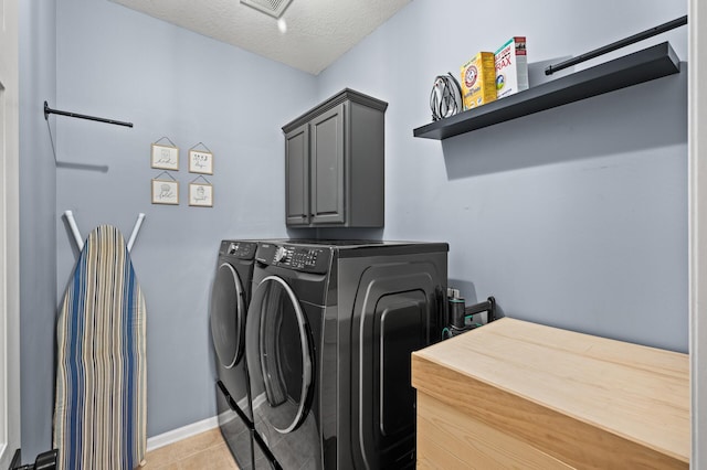 laundry room with cabinet space, light tile patterned floors, baseboards, washing machine and clothes dryer, and a textured ceiling