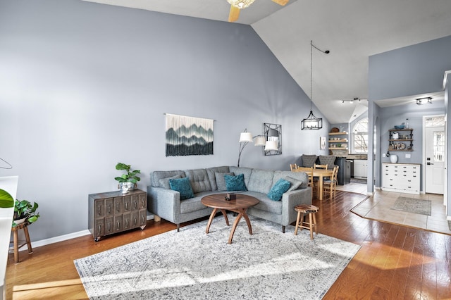 living area featuring ceiling fan, high vaulted ceiling, baseboards, and hardwood / wood-style floors