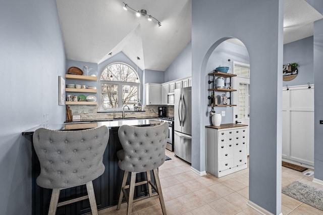 kitchen with light tile patterned flooring, open shelves, appliances with stainless steel finishes, a sink, and a peninsula
