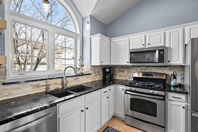 kitchen with appliances with stainless steel finishes, a sink, white cabinetry, lofted ceiling, and backsplash