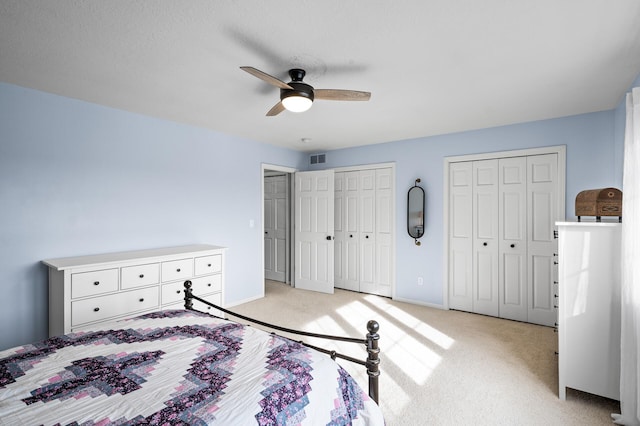 bedroom with a ceiling fan, visible vents, light colored carpet, baseboards, and two closets
