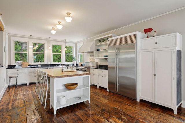 kitchen with a center island, custom range hood, white cabinets, wood counters, and stainless steel built in fridge