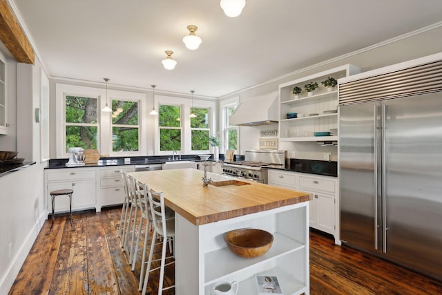 kitchen featuring stainless steel appliances, premium range hood, butcher block counters, and white cabinetry